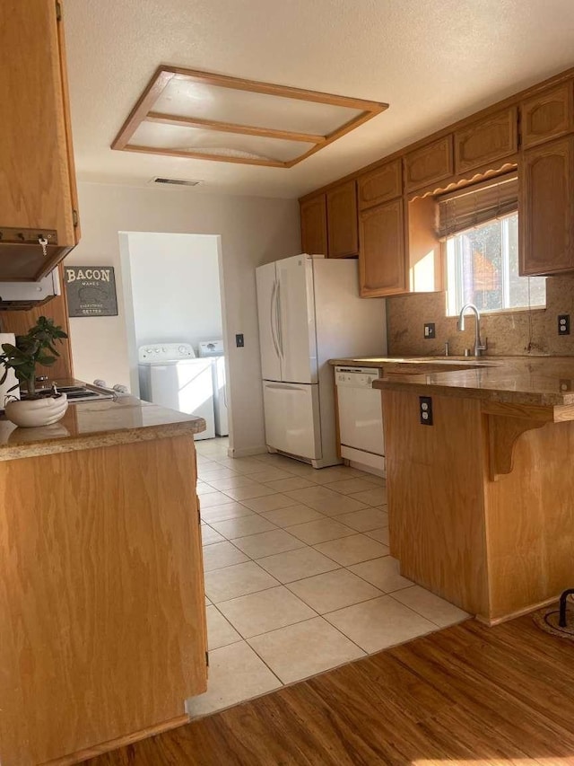 kitchen with white appliances, a peninsula, brown cabinets, backsplash, and washer and clothes dryer