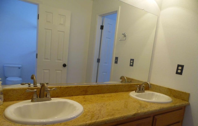 bathroom with double vanity, toilet, and a sink