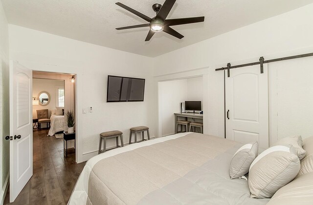 bedroom featuring a ceiling fan, dark wood-style flooring, a textured ceiling, and a barn door