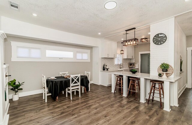 kitchen with a peninsula, a kitchen breakfast bar, white cabinets, dark wood-style floors, and decorative light fixtures