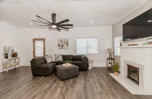 living area with a brick fireplace, plenty of natural light, a textured ceiling, and wood finished floors