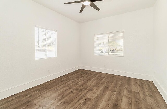 empty room with dark wood-type flooring, a ceiling fan, and baseboards