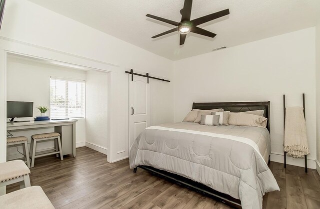 bedroom with ceiling fan, a barn door, wood finished floors, visible vents, and baseboards