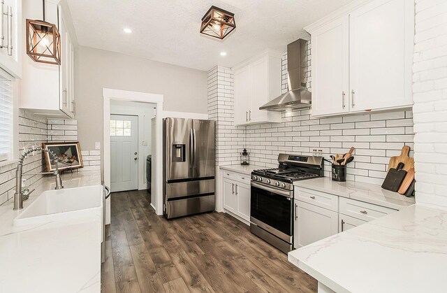 kitchen featuring light stone counters, stainless steel appliances, dark wood-style flooring, white cabinetry, and wall chimney exhaust hood