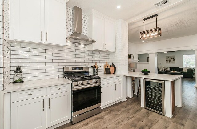 kitchen with wine cooler, visible vents, light countertops, stainless steel gas range oven, and wall chimney exhaust hood