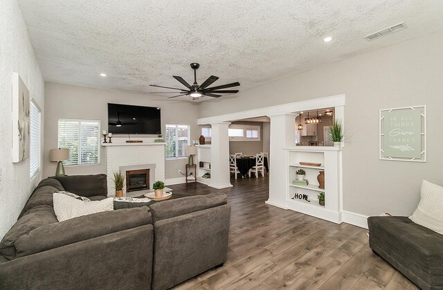 living room featuring decorative columns, visible vents, a brick fireplace, a textured ceiling, and wood finished floors