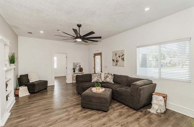 living area with a textured ceiling, ceiling fan, wood finished floors, visible vents, and baseboards