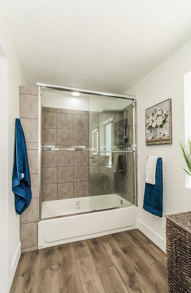 full bath with a textured ceiling, combined bath / shower with glass door, wood finished floors, and baseboards