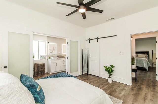 bedroom with a barn door, baseboards, visible vents, dark wood-style flooring, and a sink