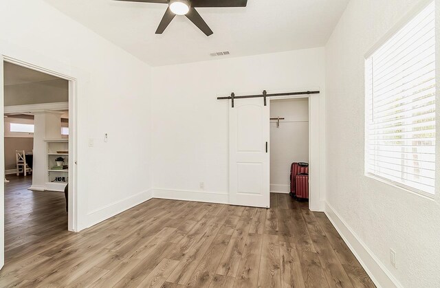 unfurnished room featuring a barn door, wood finished floors, a ceiling fan, and baseboards