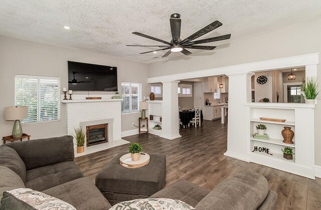 living area featuring ceiling fan, a fireplace, dark wood finished floors, and ornate columns