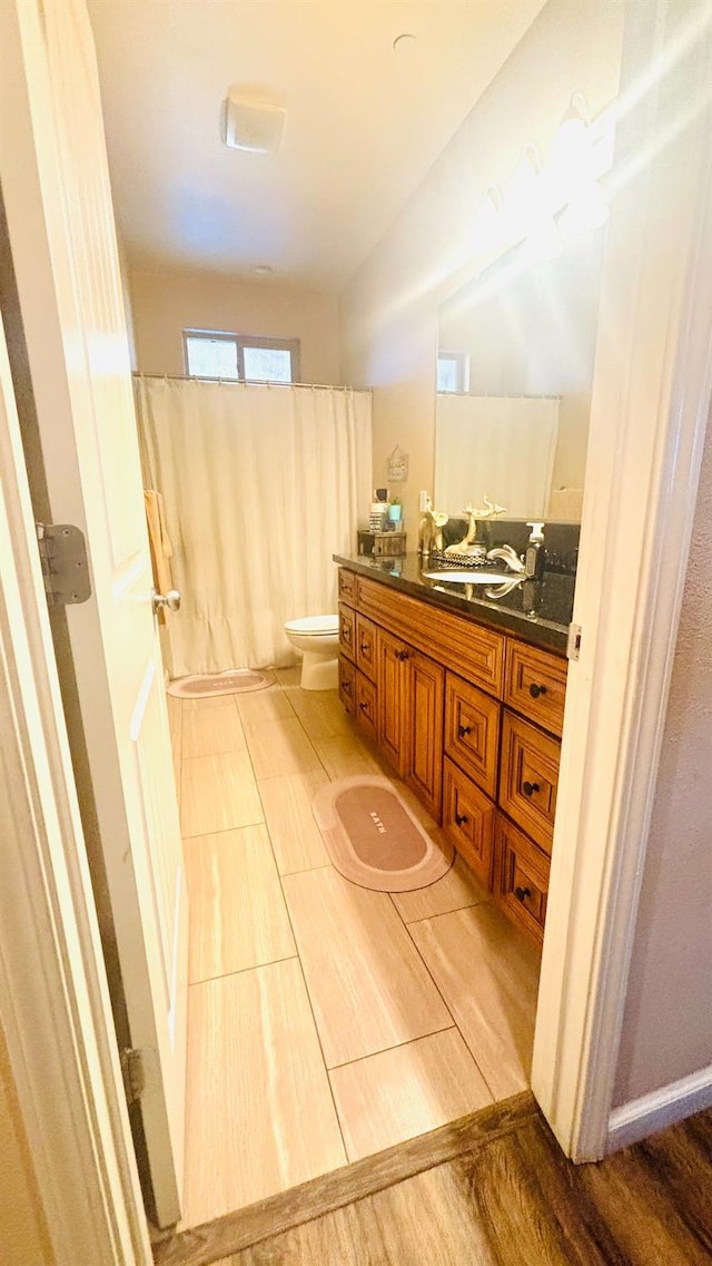 full bath with toilet, a shower with curtain, wood finished floors, and vanity