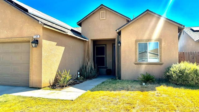 entrance to property with an attached garage, fence, roof mounted solar panels, and stucco siding