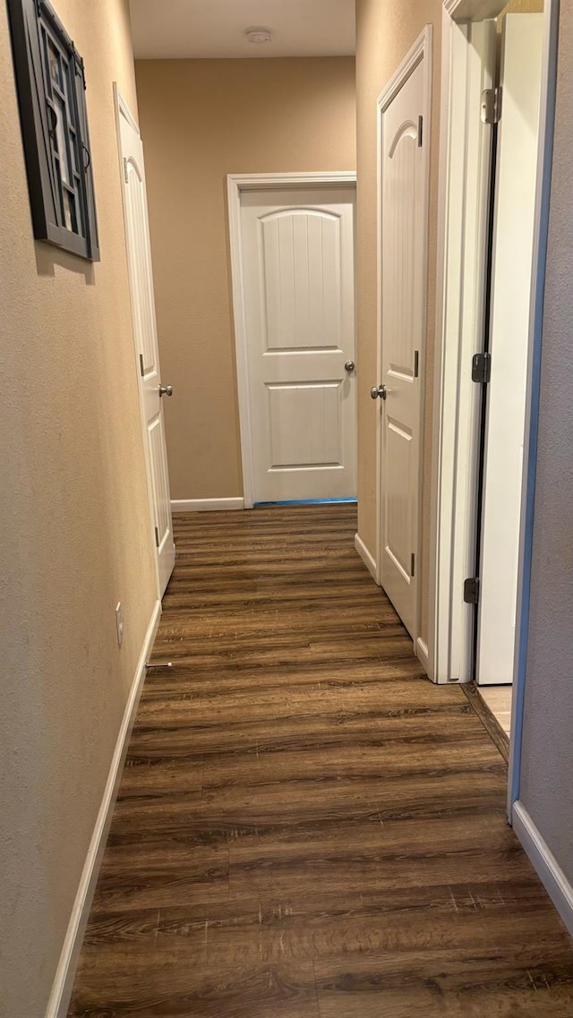 corridor with dark wood-style flooring and baseboards