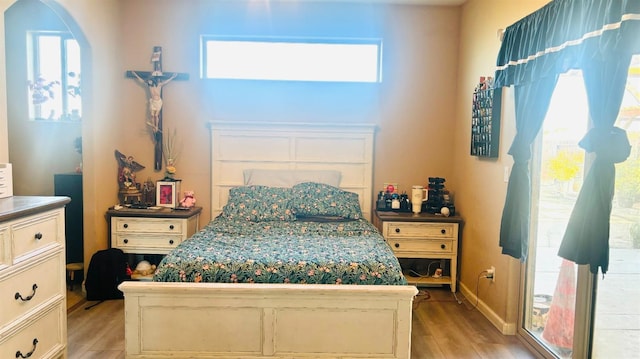 bedroom featuring arched walkways, baseboards, multiple windows, and light wood finished floors