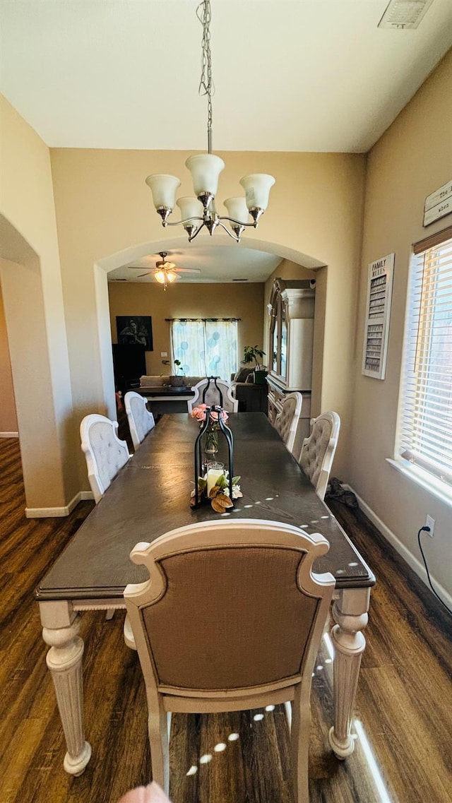 dining area with ceiling fan with notable chandelier, arched walkways, baseboards, and wood finished floors