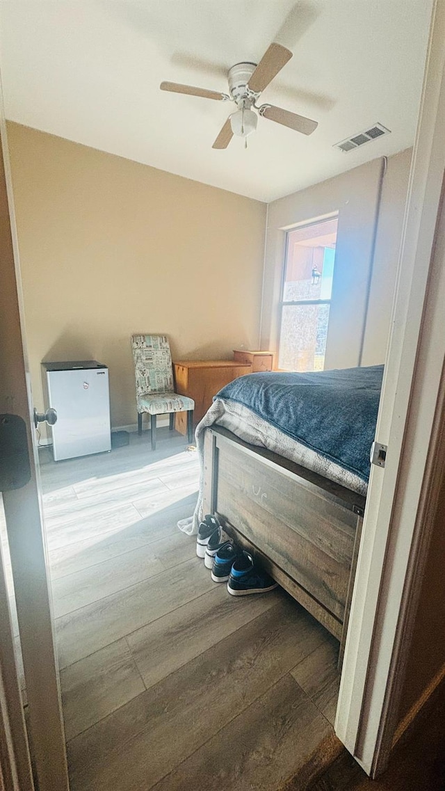 bedroom featuring ceiling fan, fridge, wood finished floors, and visible vents