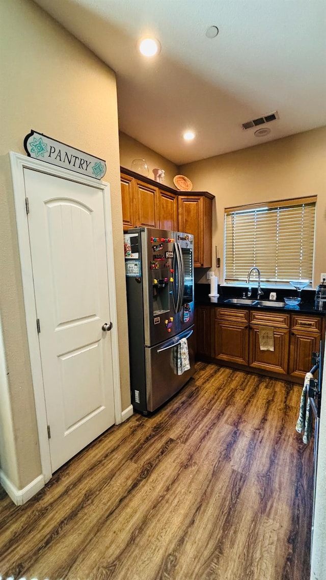 kitchen featuring visible vents, brown cabinetry, dark wood finished floors, stainless steel fridge with ice dispenser, and a sink