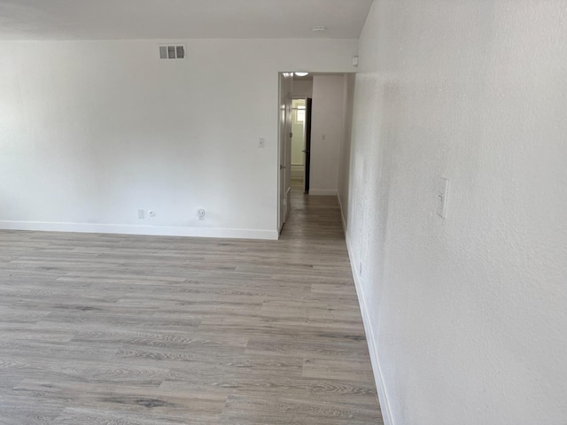 empty room with light wood-type flooring, visible vents, and baseboards