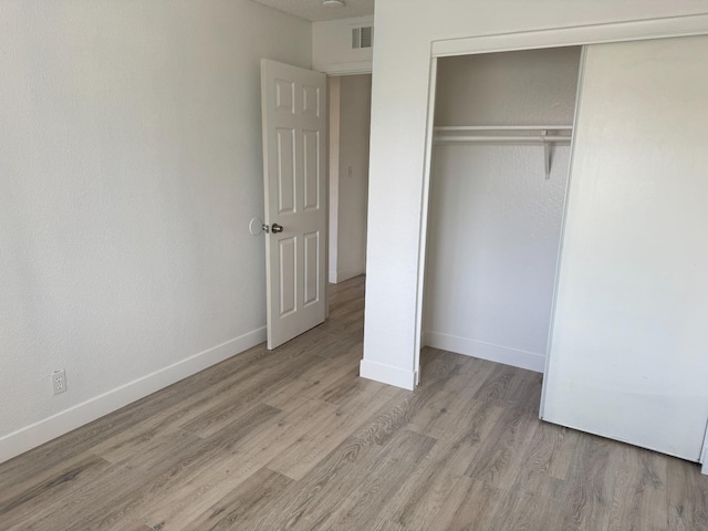 unfurnished bedroom with baseboards, a closet, visible vents, and wood finished floors