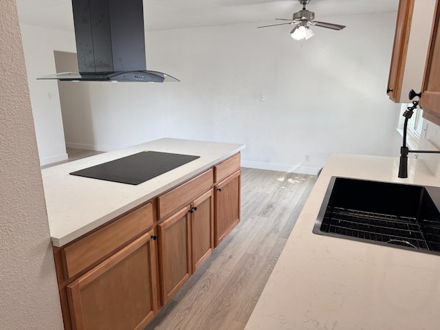 kitchen featuring brown cabinets, black electric stovetop, light countertops, light wood-style flooring, and island range hood