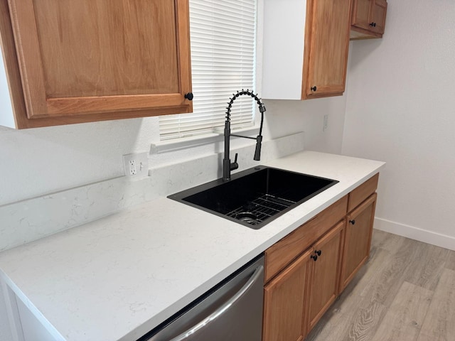 kitchen featuring light wood finished floors, baseboards, light countertops, stainless steel dishwasher, and a sink