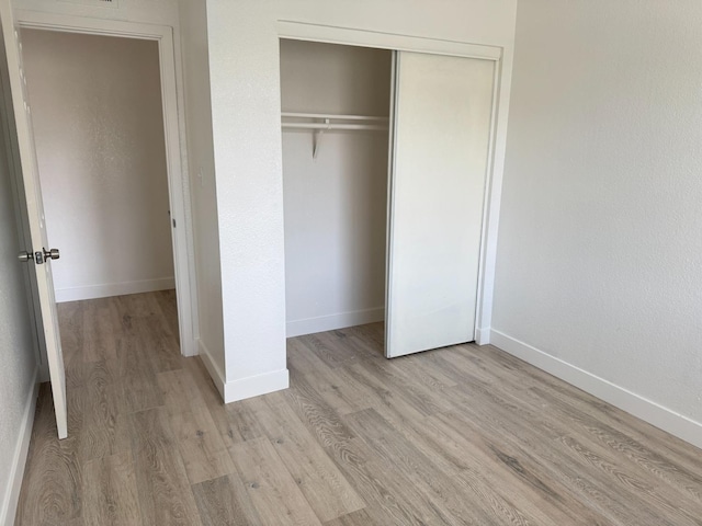 unfurnished bedroom featuring light wood finished floors, baseboards, and a closet