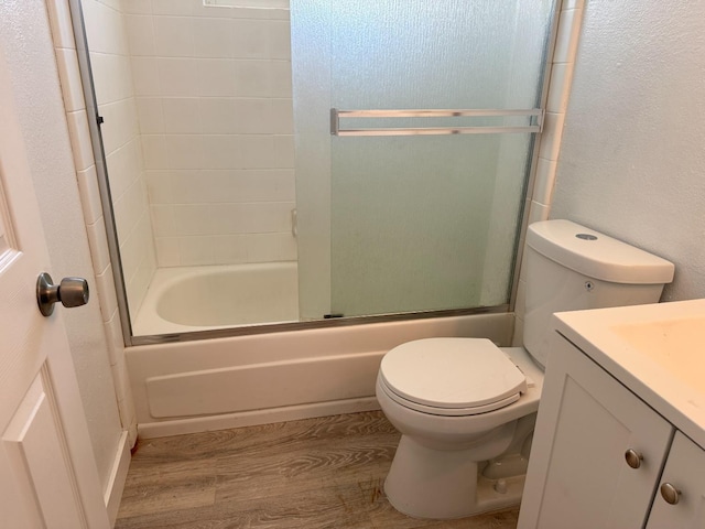 bathroom featuring toilet, enclosed tub / shower combo, wood finished floors, and vanity