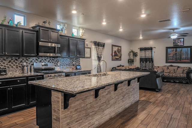 kitchen featuring appliances with stainless steel finishes, hardwood / wood-style floors, a breakfast bar area, and a center island with sink