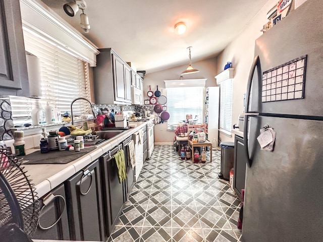 kitchen featuring tile counters, sink, vaulted ceiling, hanging light fixtures, and stainless steel appliances