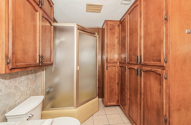 bathroom with tile patterned flooring, backsplash, a textured ceiling, an enclosed shower, and toilet