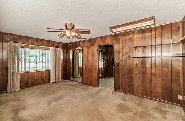 carpeted empty room featuring ceiling fan, a textured ceiling, and wooden walls