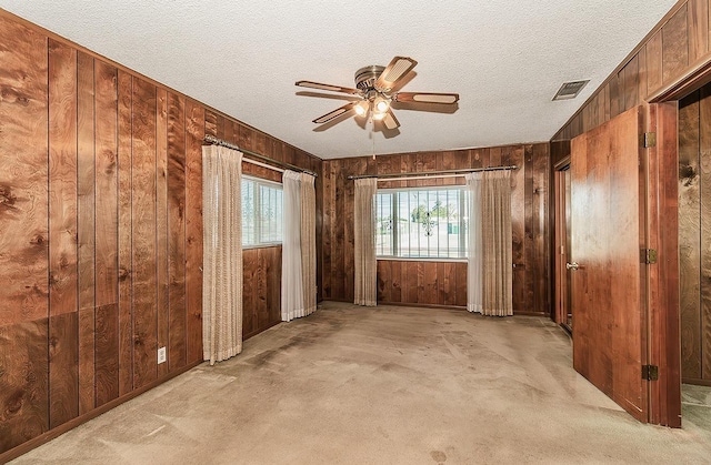 carpeted empty room featuring a textured ceiling, ceiling fan, and wooden walls