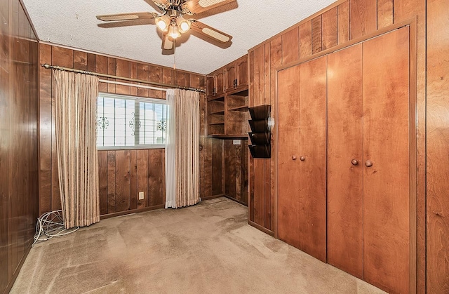 interior space with light colored carpet, a textured ceiling, and wooden walls