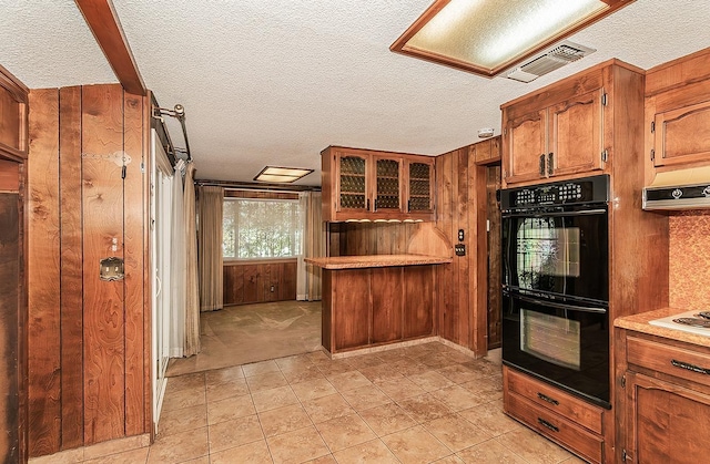 kitchen featuring double oven, wooden walls, a textured ceiling, and ventilation hood