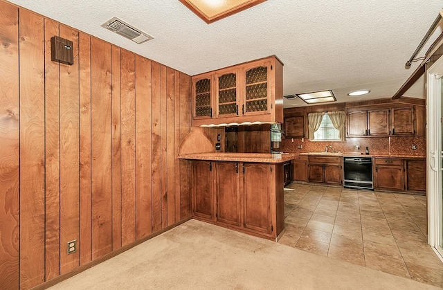 kitchen with decorative backsplash, wooden walls, kitchen peninsula, a textured ceiling, and light carpet