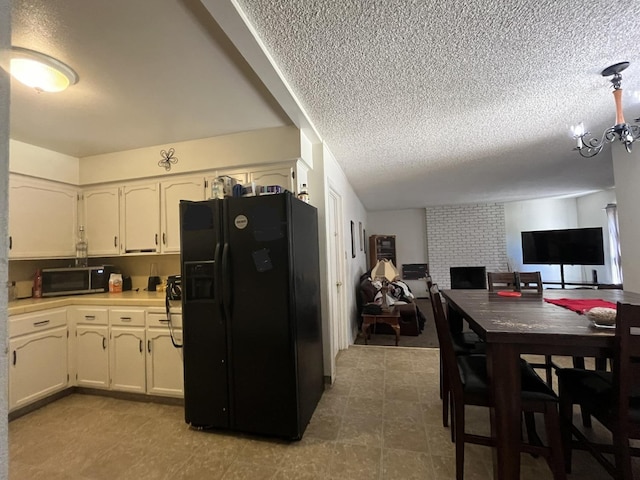 kitchen featuring a fireplace, a textured ceiling, white cabinets, and black refrigerator with ice dispenser