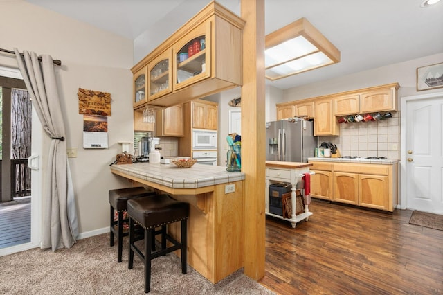 kitchen featuring white appliances, backsplash, dark hardwood / wood-style floors, tile counters, and a breakfast bar area