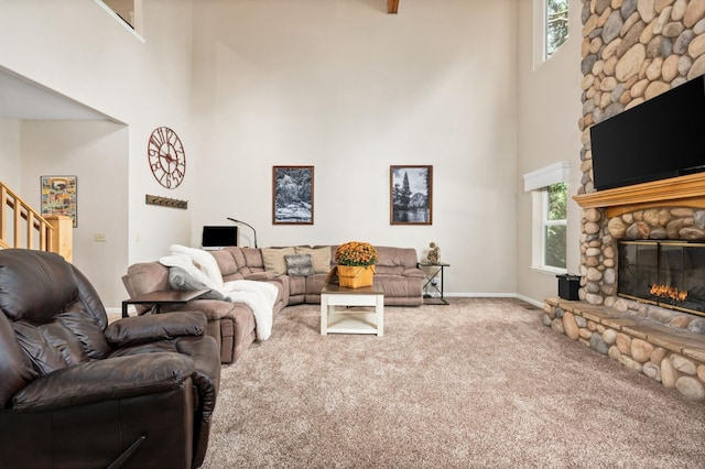 living room featuring a stone fireplace, carpet flooring, a towering ceiling, and a wealth of natural light