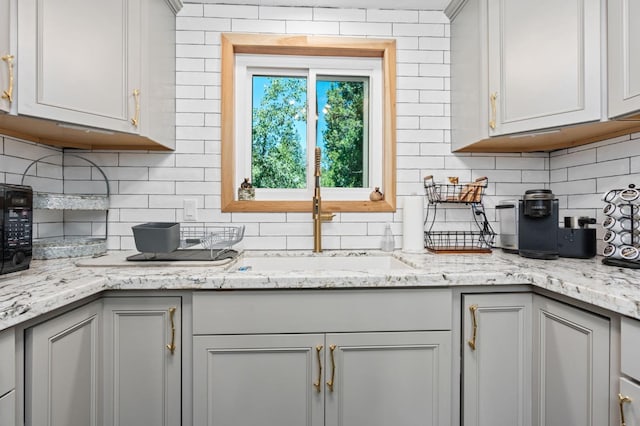 kitchen featuring gray cabinets, backsplash, light stone counters, and sink