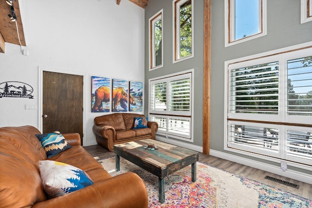 living room with plenty of natural light, a towering ceiling, beam ceiling, and hardwood / wood-style flooring