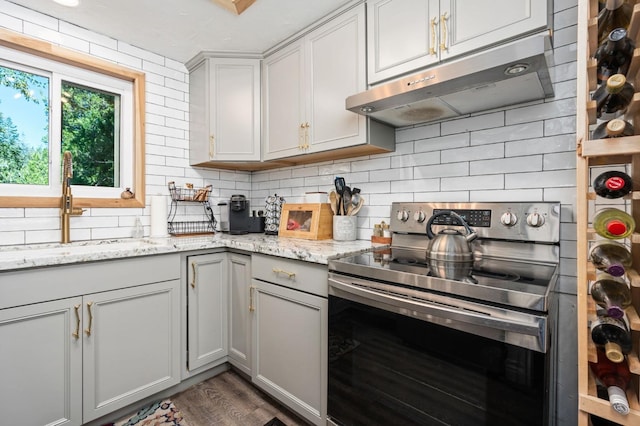 kitchen featuring stainless steel electric stove, hardwood / wood-style floors, tasteful backsplash, sink, and light stone counters