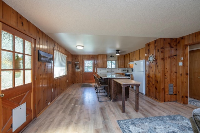 dining area with wooden walls, light hardwood / wood-style flooring, a textured ceiling, and ceiling fan