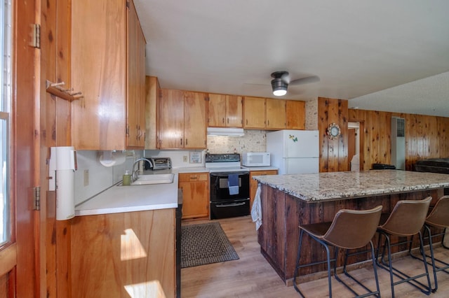 kitchen featuring a breakfast bar area, wood walls, light wood-type flooring, and white appliances