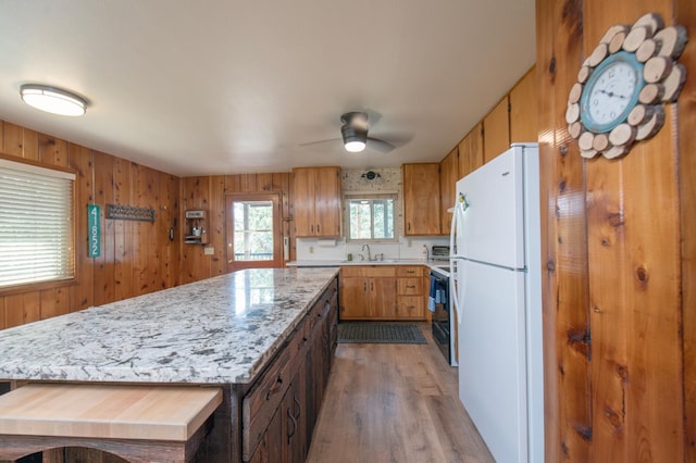 kitchen featuring ceiling fan, wood-type flooring, wood walls, sink, and white refrigerator