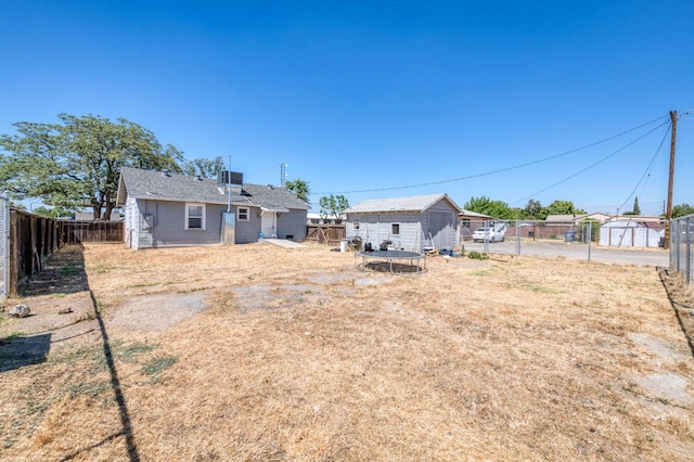 rear view of property with cooling unit, a storage shed, and a trampoline