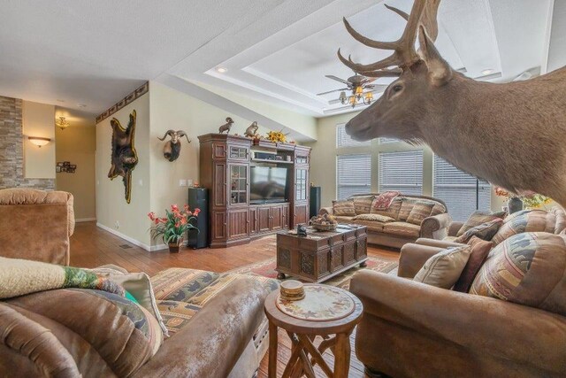 living room with baseboards, ceiling fan, a tray ceiling, and light wood finished floors