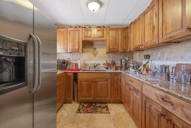 kitchen with stainless steel fridge with ice dispenser, light stone counters, sink, and decorative backsplash