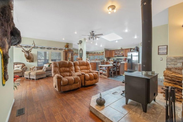 living area with a wood stove, a skylight, hardwood / wood-style flooring, visible vents, and a ceiling fan