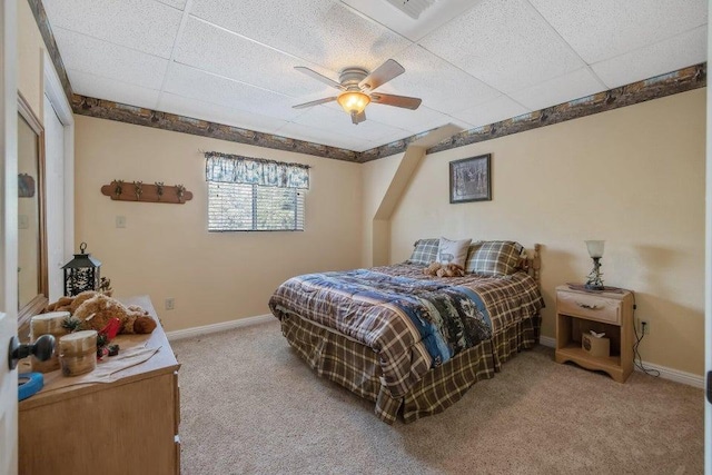 carpeted bedroom featuring baseboards, ceiling fan, and a drop ceiling